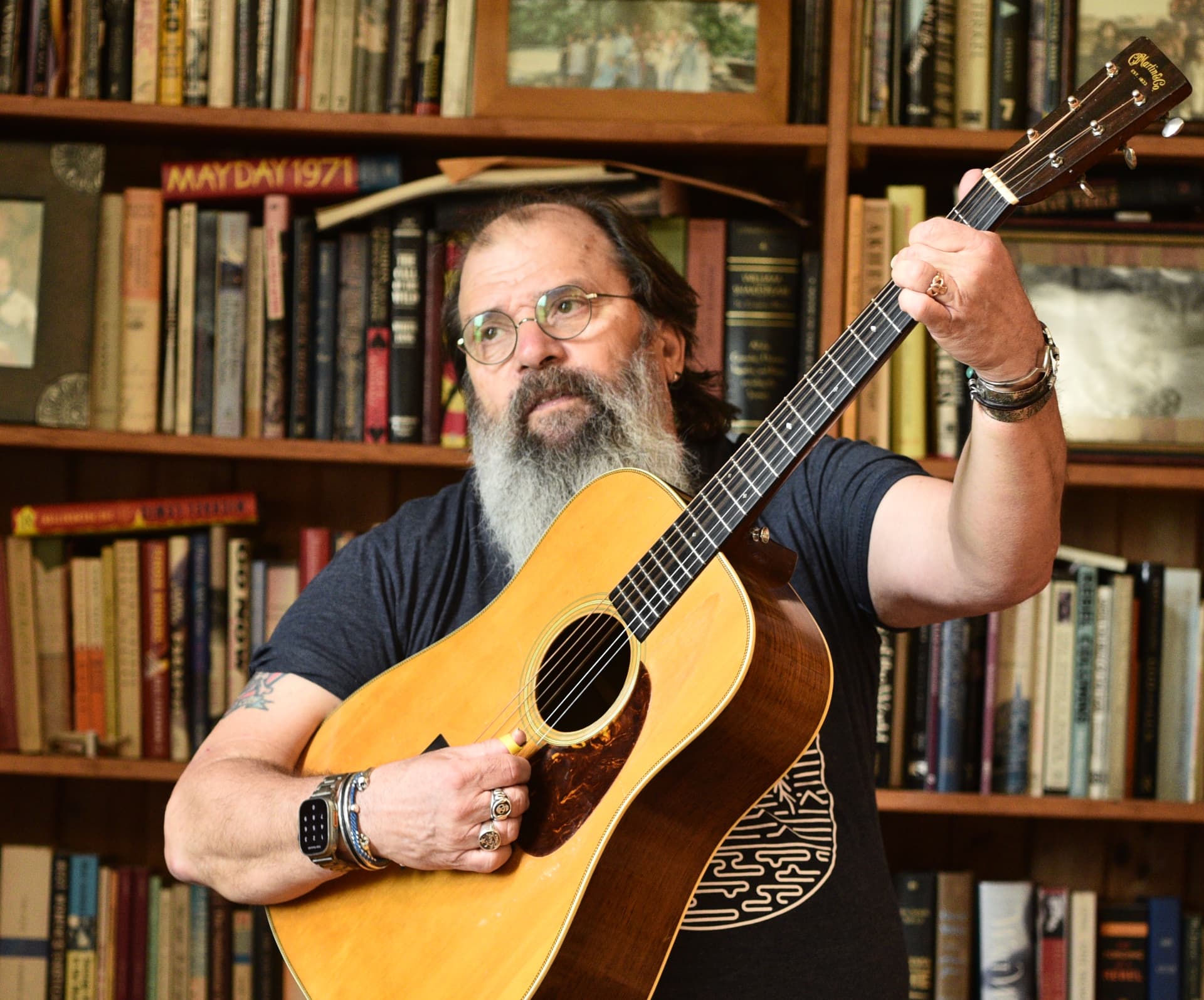 Steve Earle with his acoustic in his library.